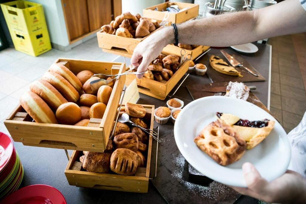 Eine Person serviert Gebäck aus Holzkisten, mit einer Schüssel Obsttorte und verschiedenen Backwaren.
