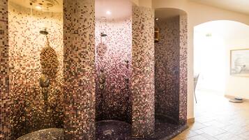 Ein Duschbereich mit Mosaikfliesen, mehreren Säulen und einem gefliesten Boden.