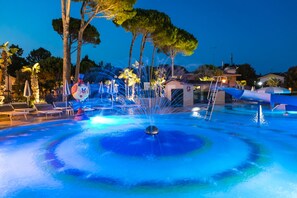 Une piscine dotée de jets d’eau, de chaises longues et d’un petit bâtiment en arrière-plan.