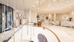A modern hotel lobby with a marble reception desk, a glass staircase, and contemporary lighting fixtures. - Hotel Mediterranee Family & Spa Hotel (San Michele al Tagliamento)