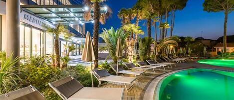 A poolside area with lounge chairs and umbrellas, surrounded by palm trees and a building with a sign that reads "MEDINA".