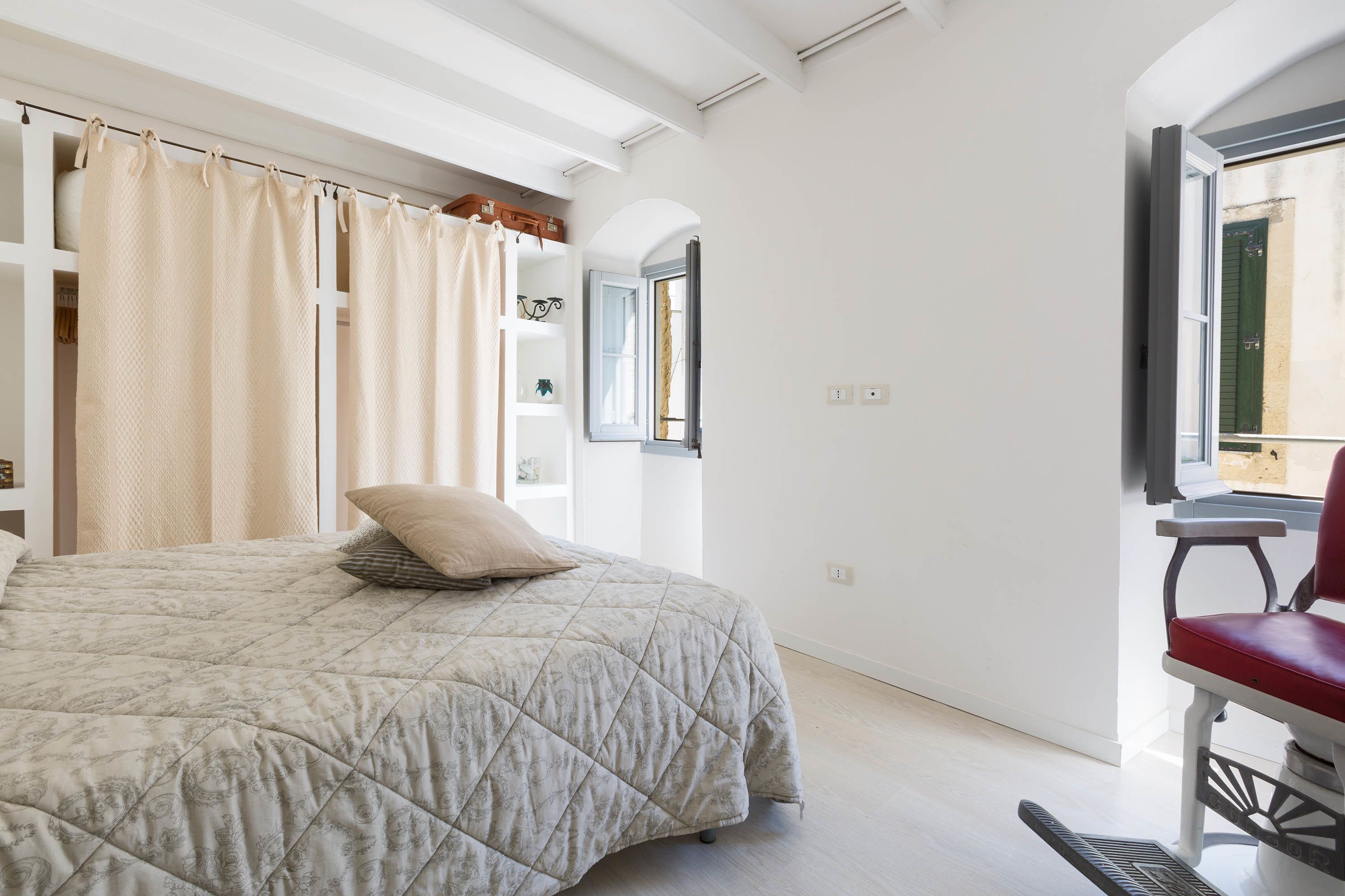 A bedroom with a bed, a chair, a window, and a door.