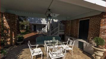 A covered patio with a brick wall, a glass table, white chairs, and a blue sofa.