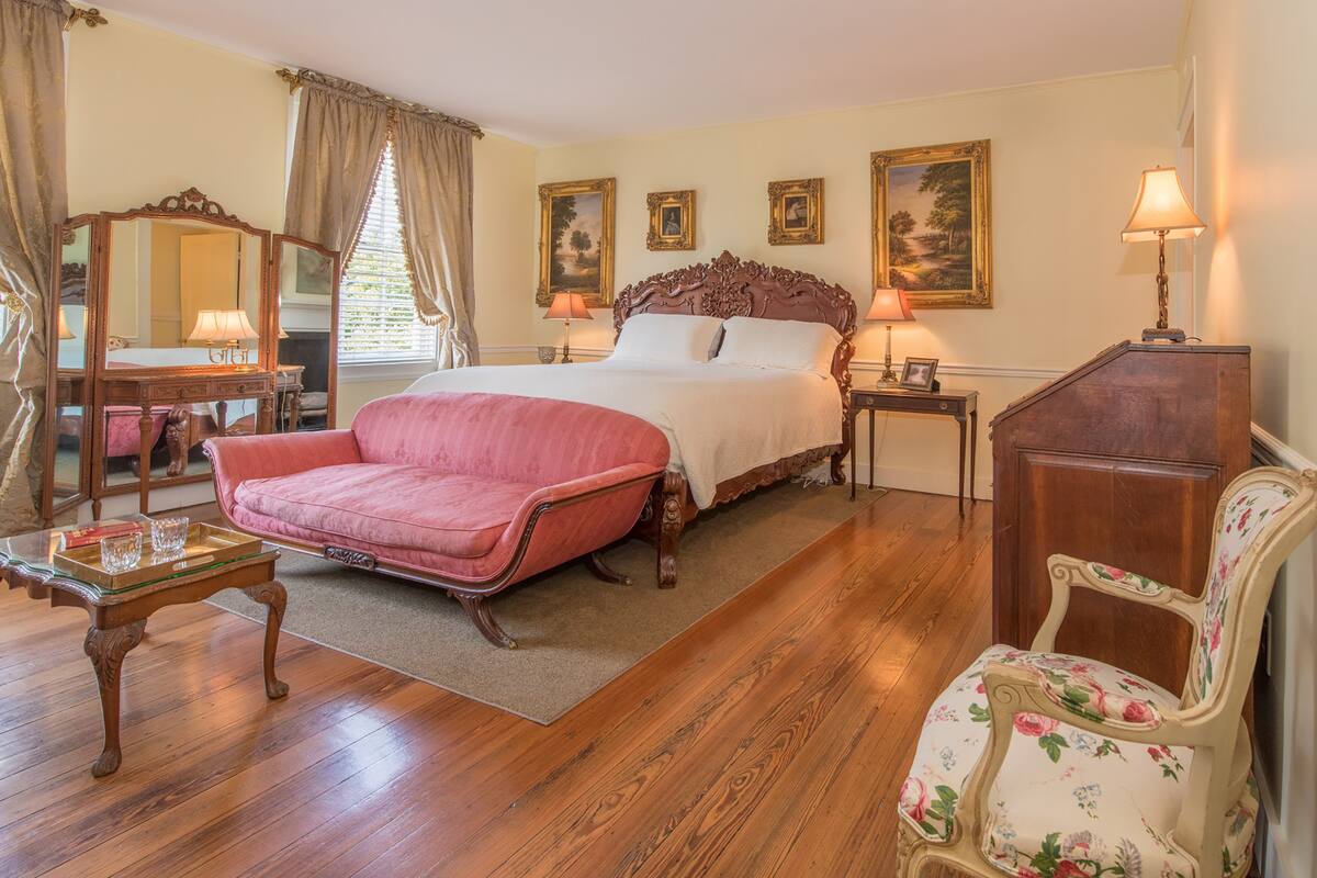 Un dormitorio con una cama grande, un sofá rosa, un aparador de madera y una silla tapizada con flores.
