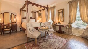 A four-poster bed with a canopy, a sitting area with a small table and chairs, and a large mirror on the wall. - The Burn Bed and Breakfast (Natchez)