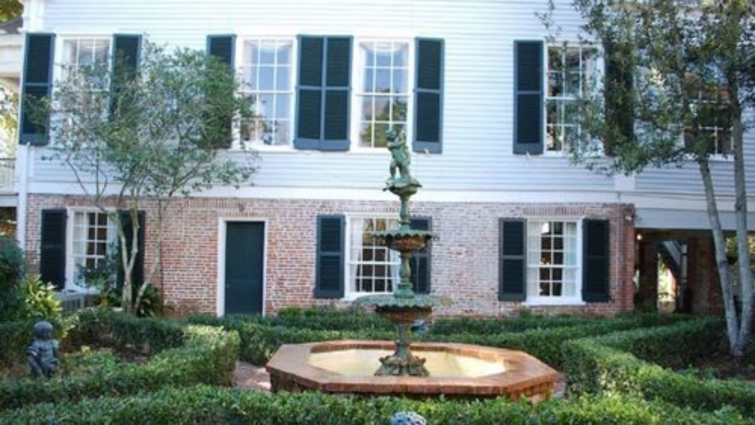 A building with a brick facade, multiple windows with shutters, and a central fountain.