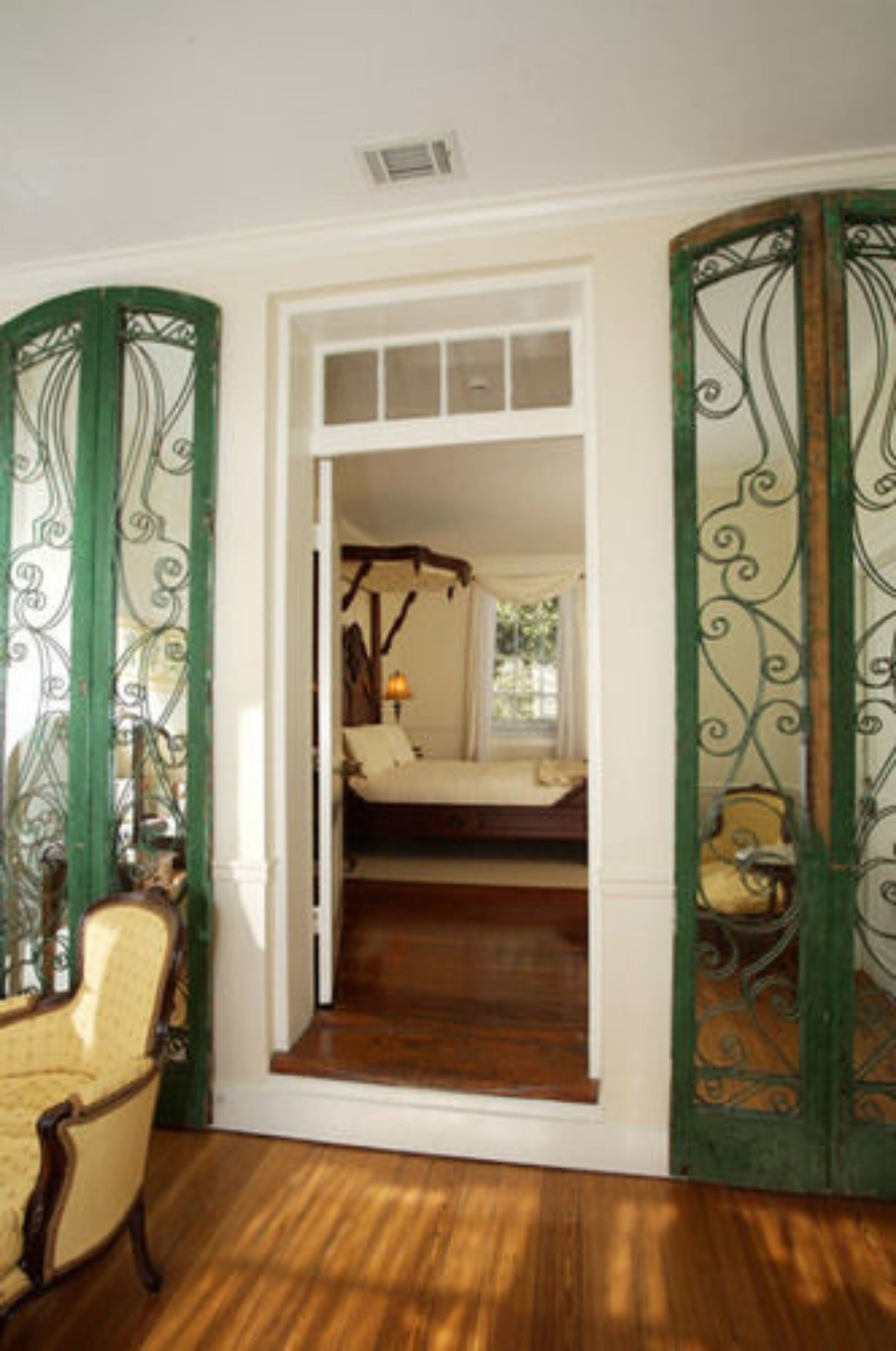 Una habitación con piso de madera, una cama con ropa de cama blanca y una ventana con cortinas.