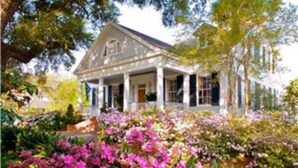A white colonial-style house with a porch, surrounded by a garden with pink flowers. - The Burn Bed and Breakfast (Natchez)