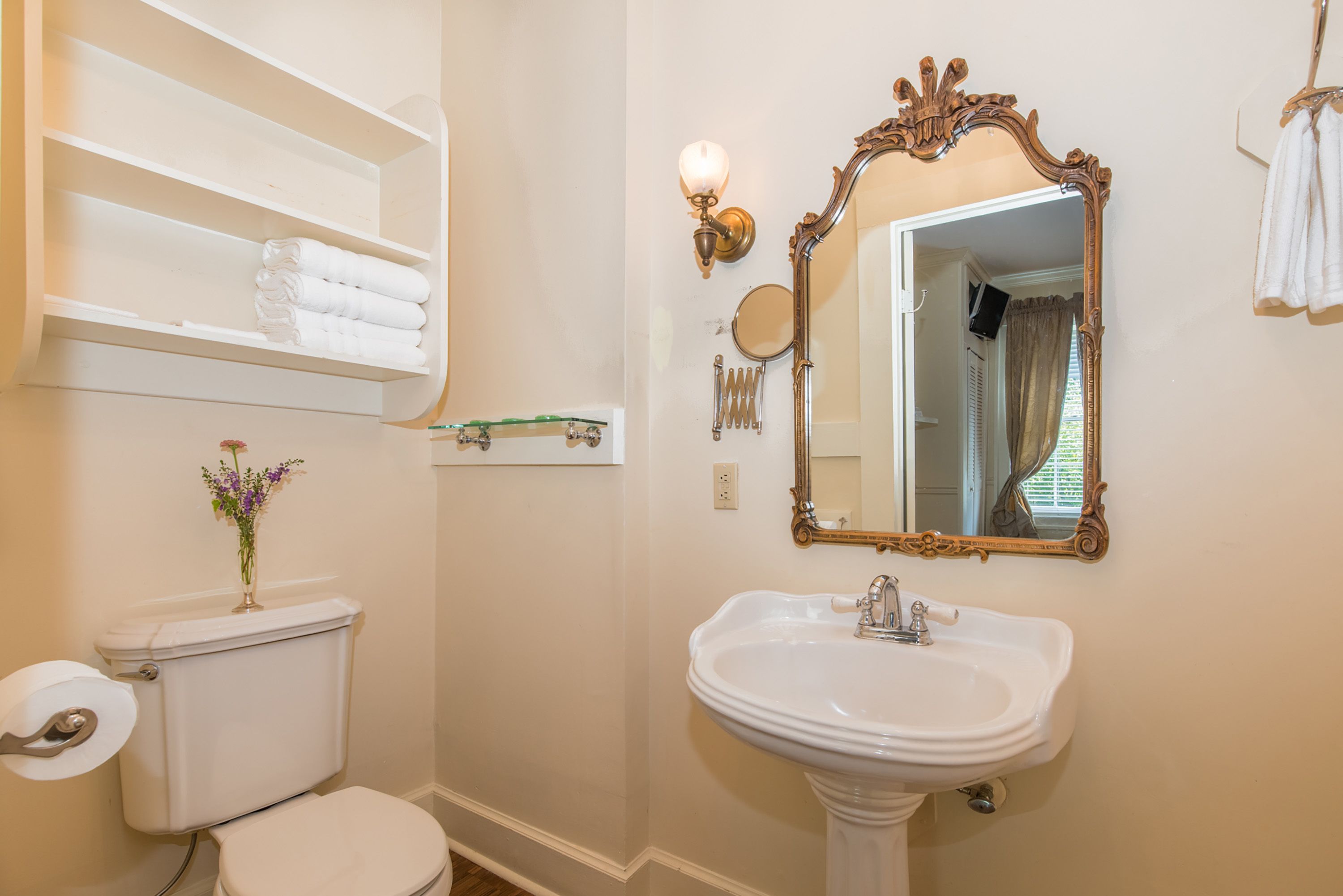 Ein Badezimmer mit Toilette, Waschbecken, Spiegel und einem Regal mit Handtüchern.