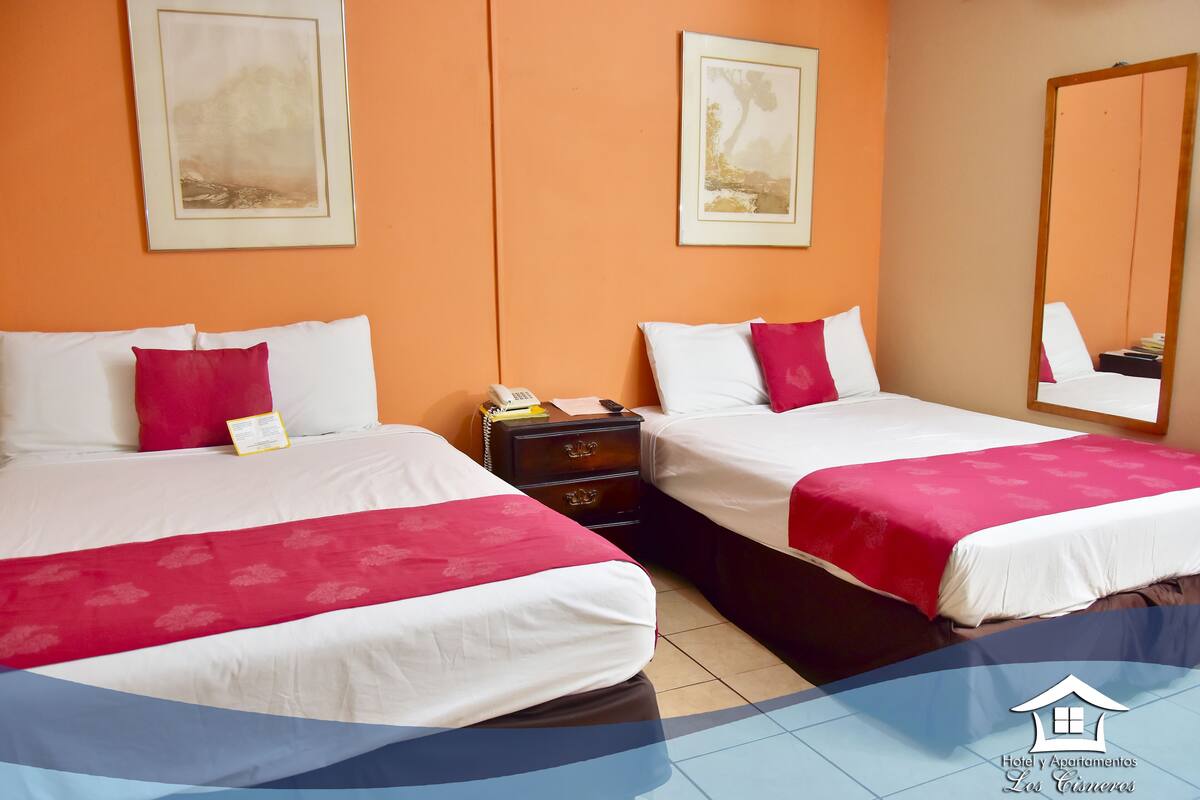 A hotel room with two beds, each with white and red bedding, a nightstand with a phone, and framed artwork on the walls.
