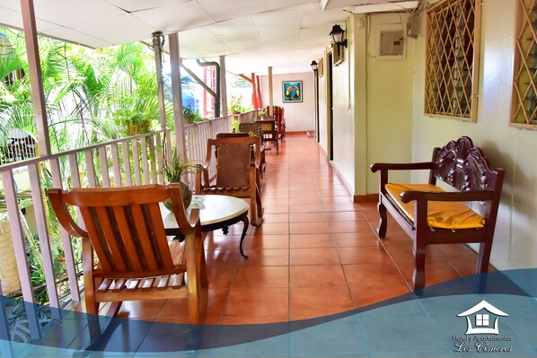 A covered outdoor area with wooden chairs and tables, a railing, and a view of greenery. - Hotel Los Cisneros (Managua)