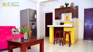 Una sala de estar con un sofá rojo, una mesa de centro de madera, y una zona de cocina con armarios amarillos y un microondas.