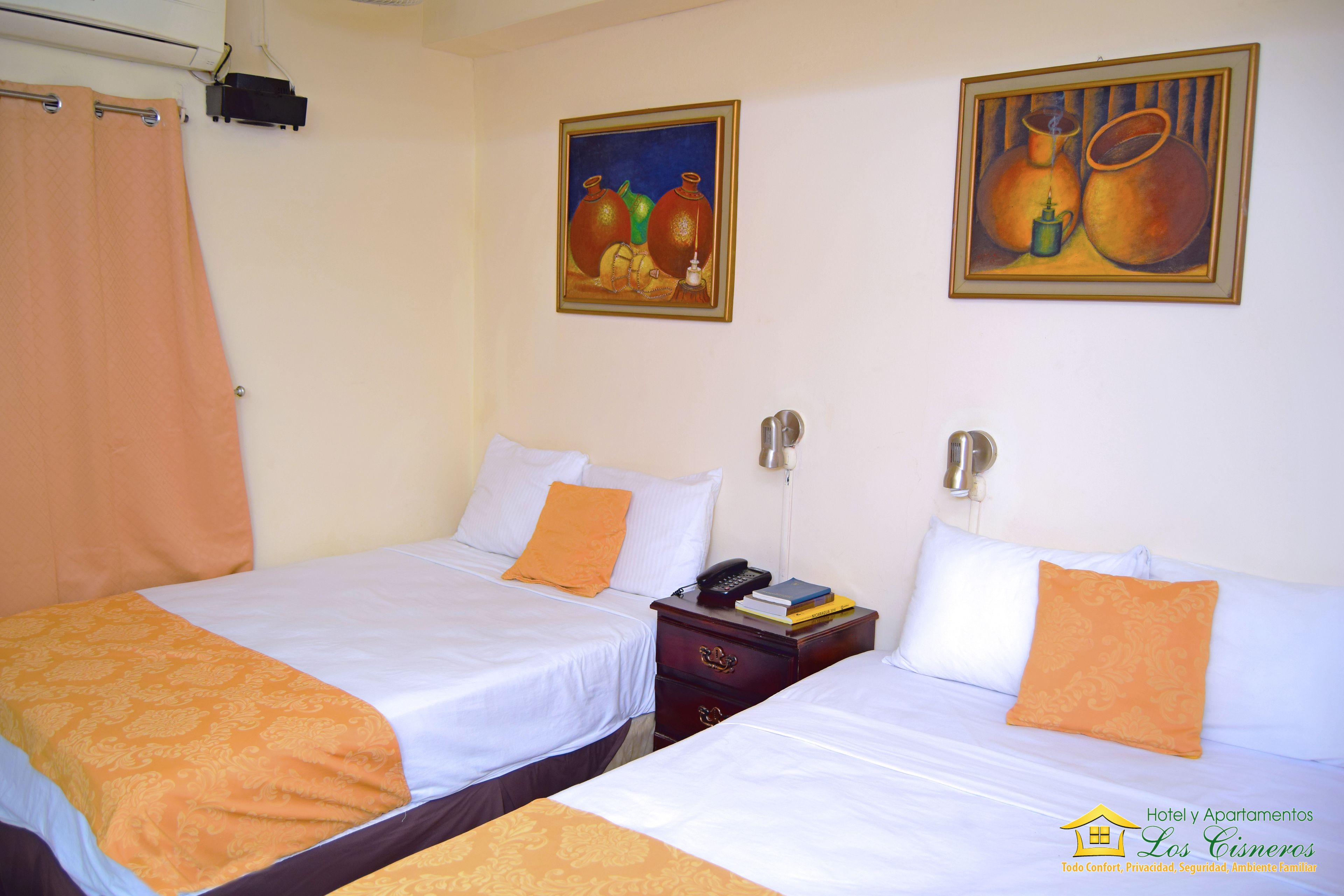 A hotel room with two beds, a nightstand, and two paintings on the wall.
