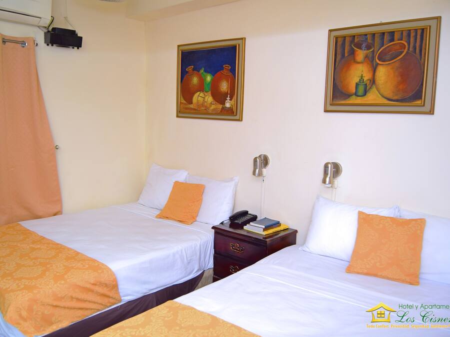 A hotel room with two beds, a nightstand, and two paintings on the wall.