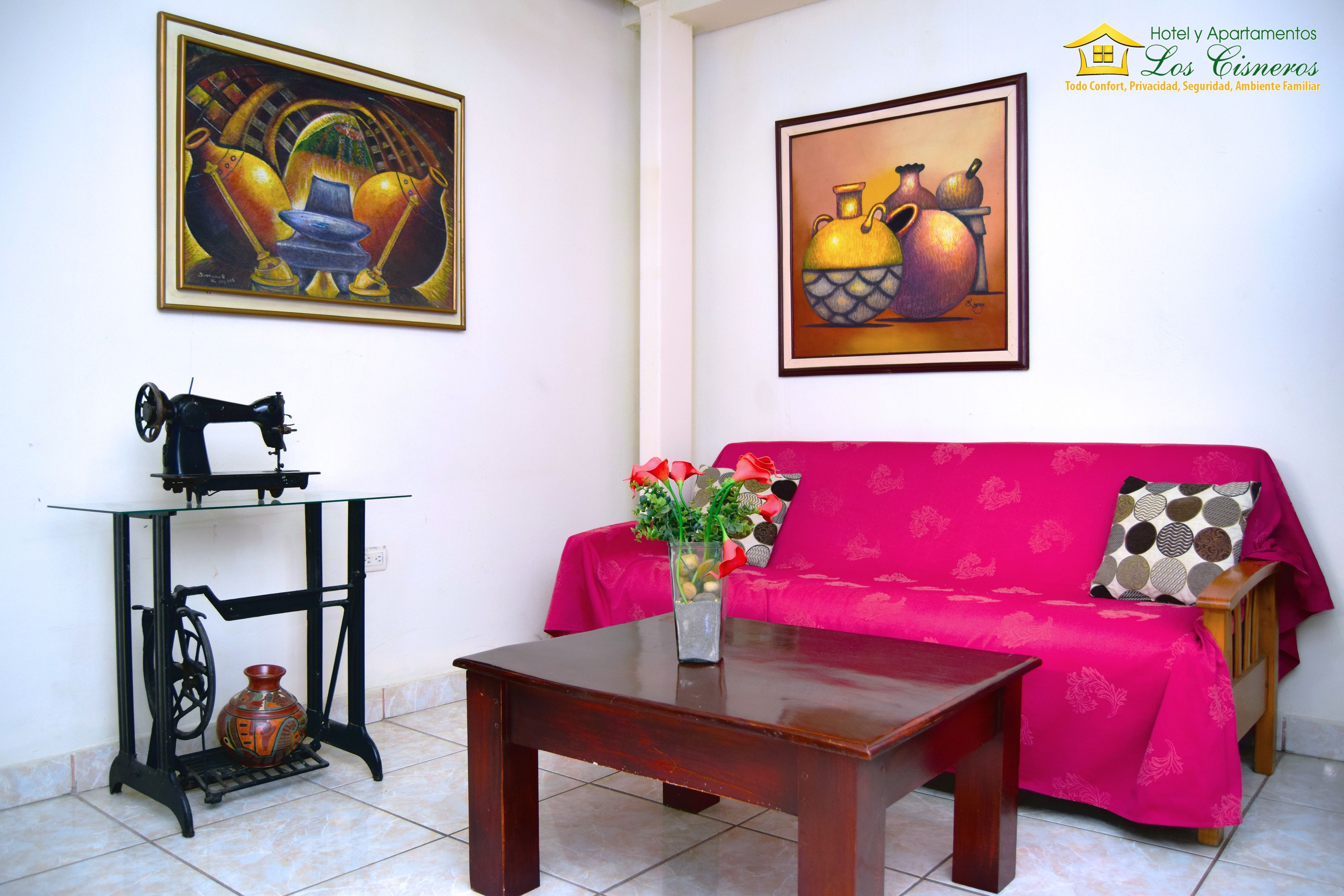 Una sala de estar con un sofá, una mesa de centro, una máquina de coser y dos cuadros en la pared.