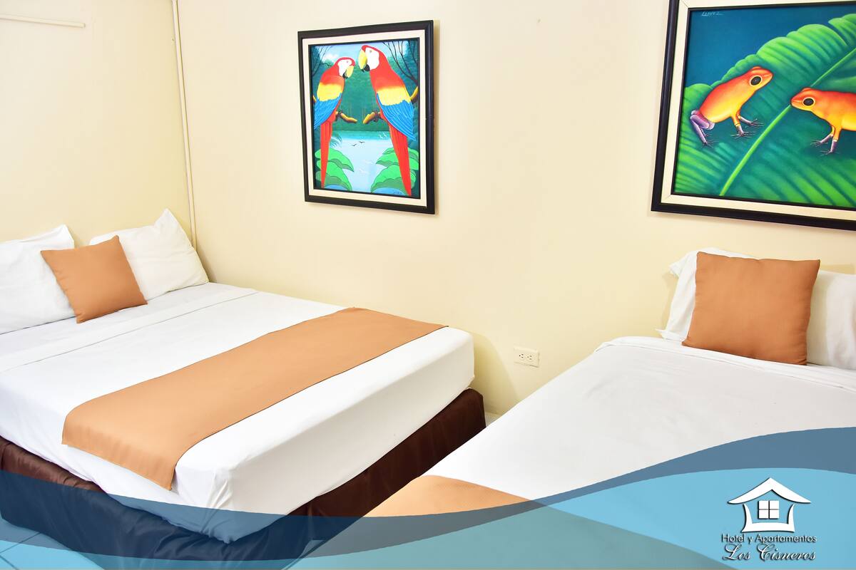 A hotel room with two beds, a framed painting of parrots, and a logo for Hotel y Apartamentos Los Caimeros.
