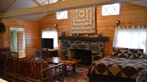 A log cabin interior with a stone fireplace, wooden furniture, and a quilted bedspread. - Red Bud Lodge (El Portal)