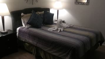 A neatly made bed with striped bedding, two bedside lamps, a decorative wall piece, and a mirror.