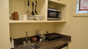 A compact kitchen with a granite countertop, a built-in microwave, a coffee maker, and a sink. - Red Bud Lodge (El Portal)