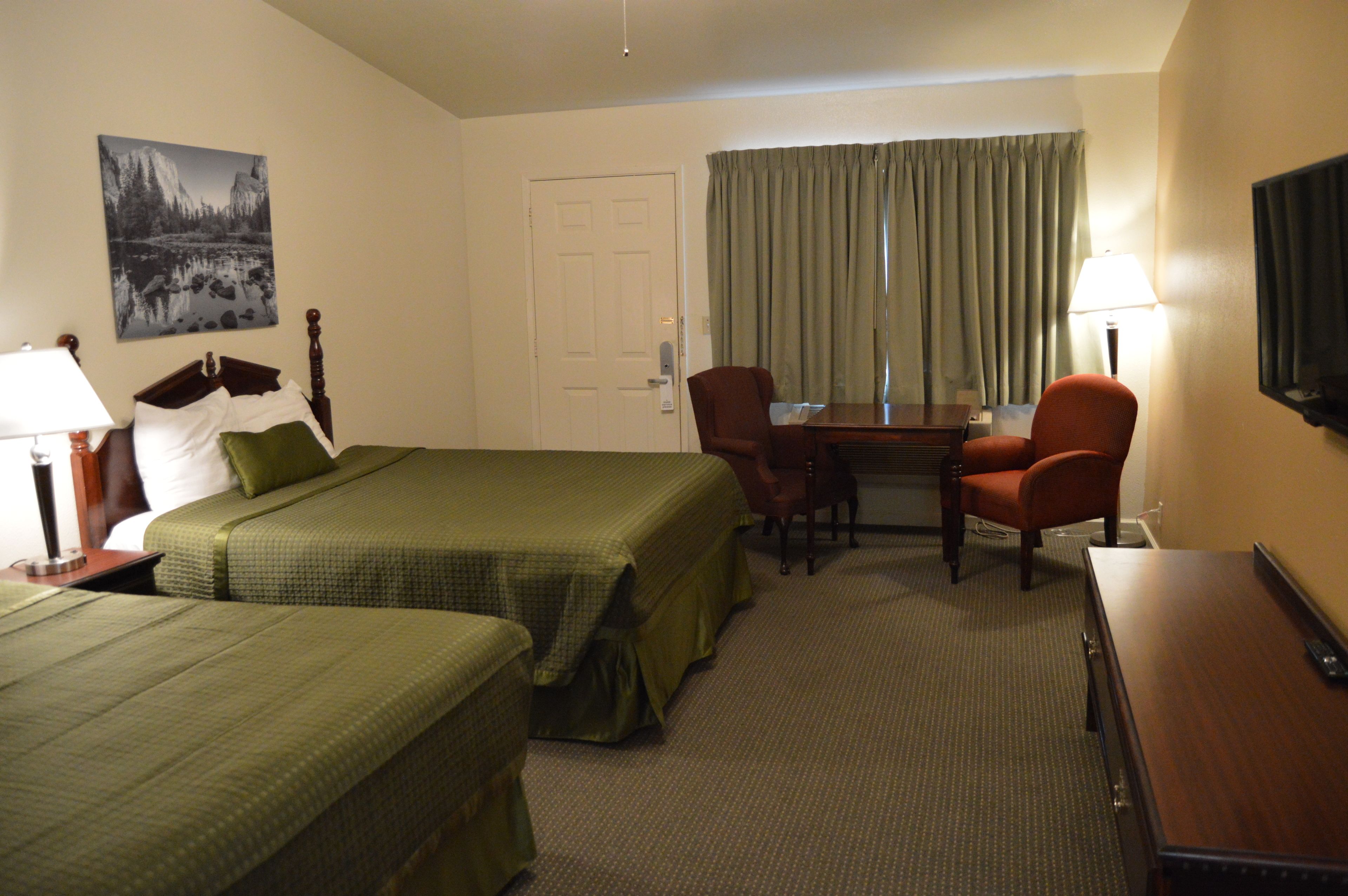 A hotel room with two beds, a desk, a chair, a TV, and a painting on the wall.