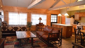 A cozy log cabin interior with a wooden sofa, a dining table, and a kitchen area. - Red Bud Lodge (El Portal)