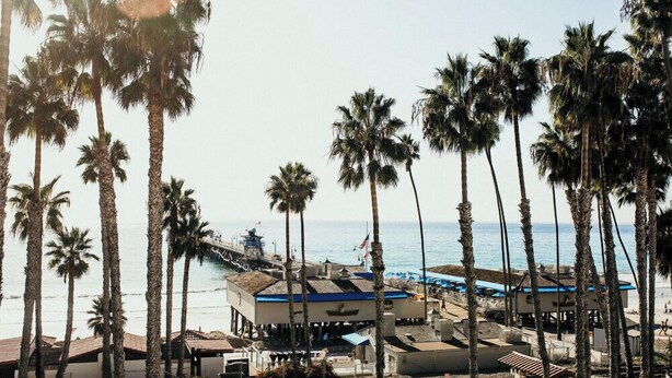 A coastal hotel with a beach view, palm trees, and a pier. - Casa Tropicana (San Clemente)