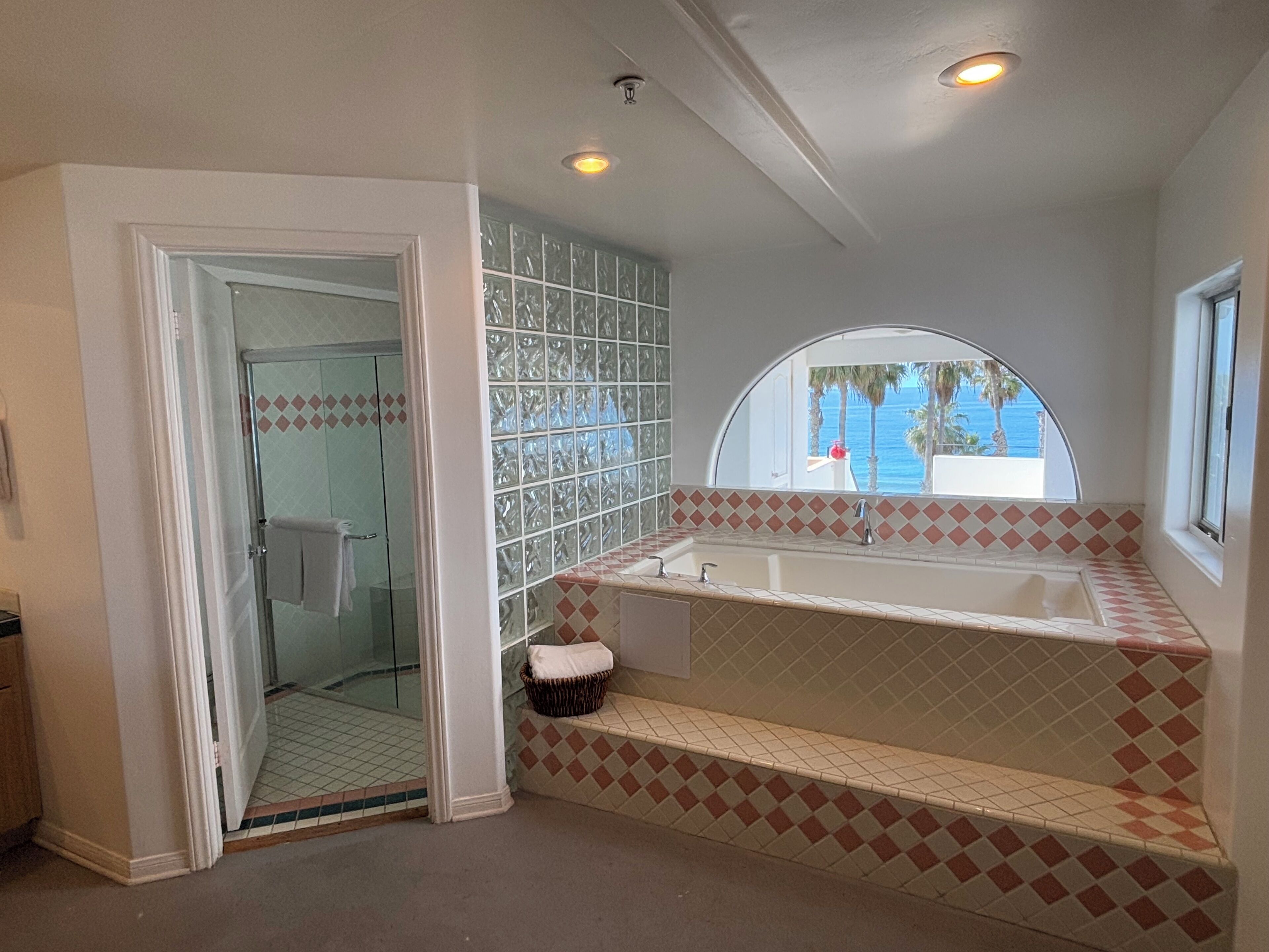 A bathroom with a glass shower enclosure, a bathtub with a view of the ocean, and a tiled backsplash.