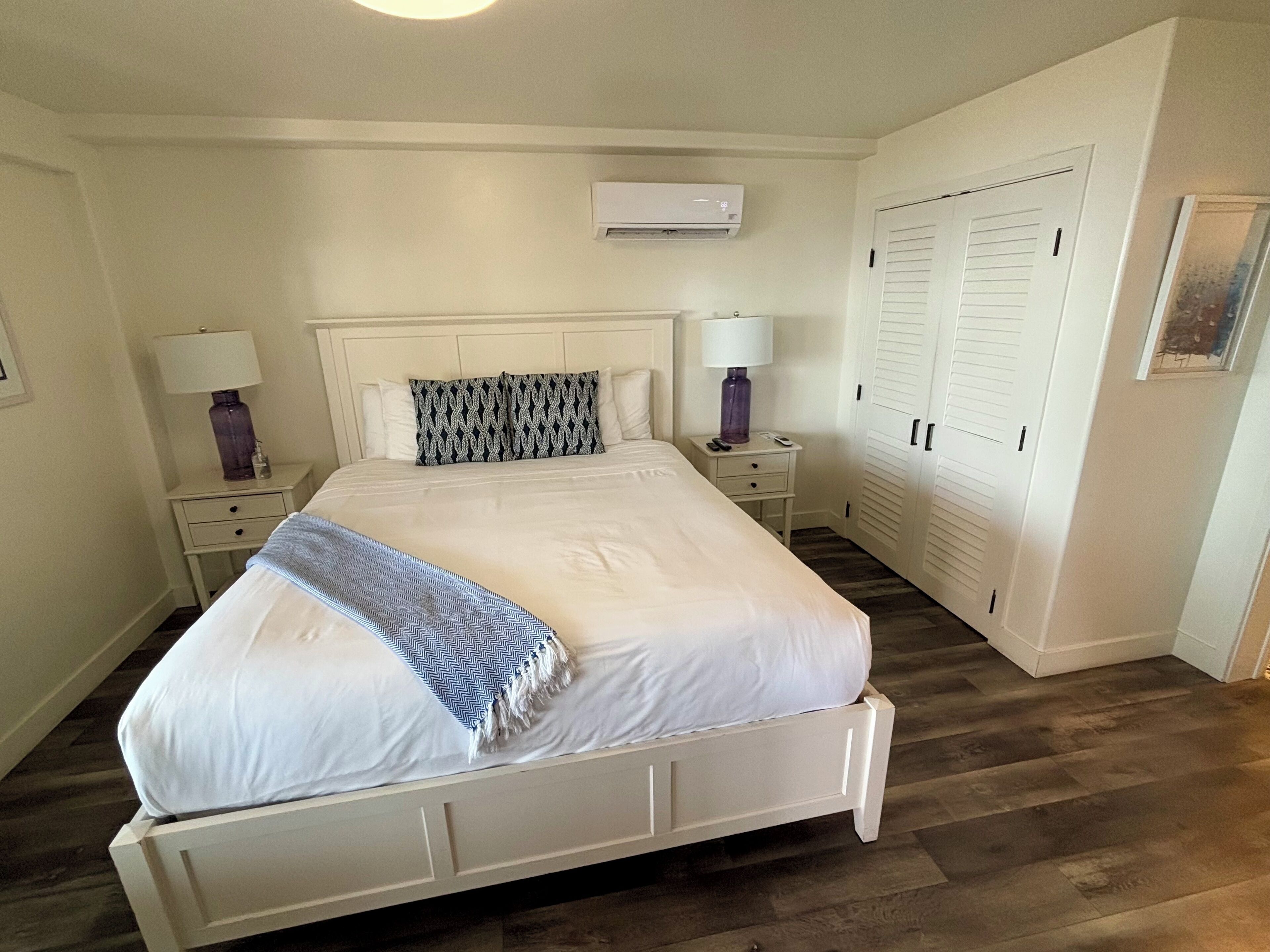 A neatly arranged bedroom with a bed, bedside tables, a wardrobe, and an air conditioning unit.