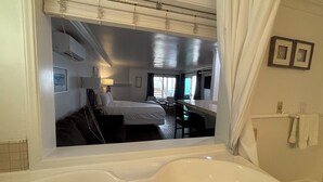 A hotel room with a large bathtub, a bed, a desk, and a view of the balcony. - Casa Tropicana (San Clemente)