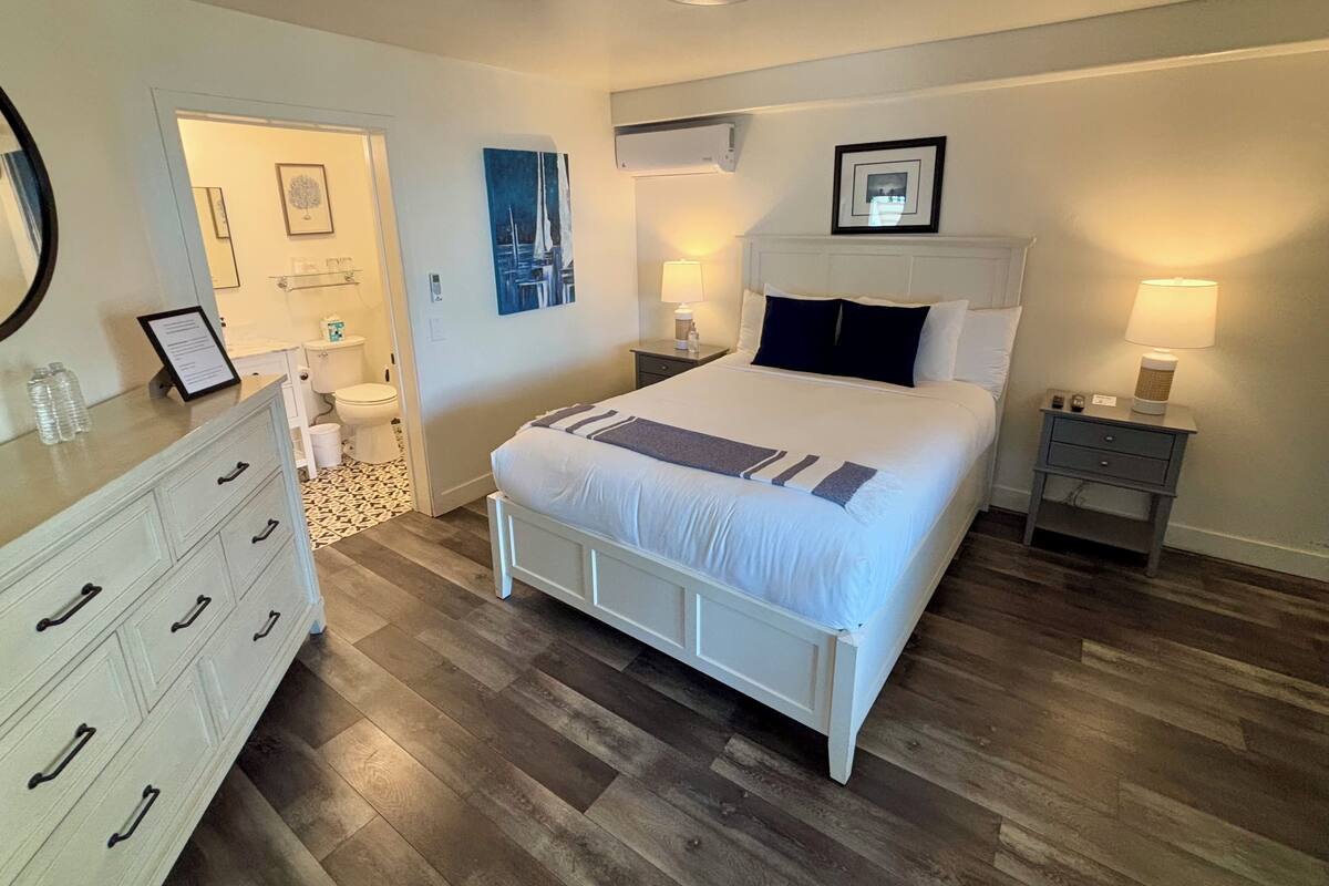 Quarto com cama, cômoda, mesas de cabeceira e banheiro.
