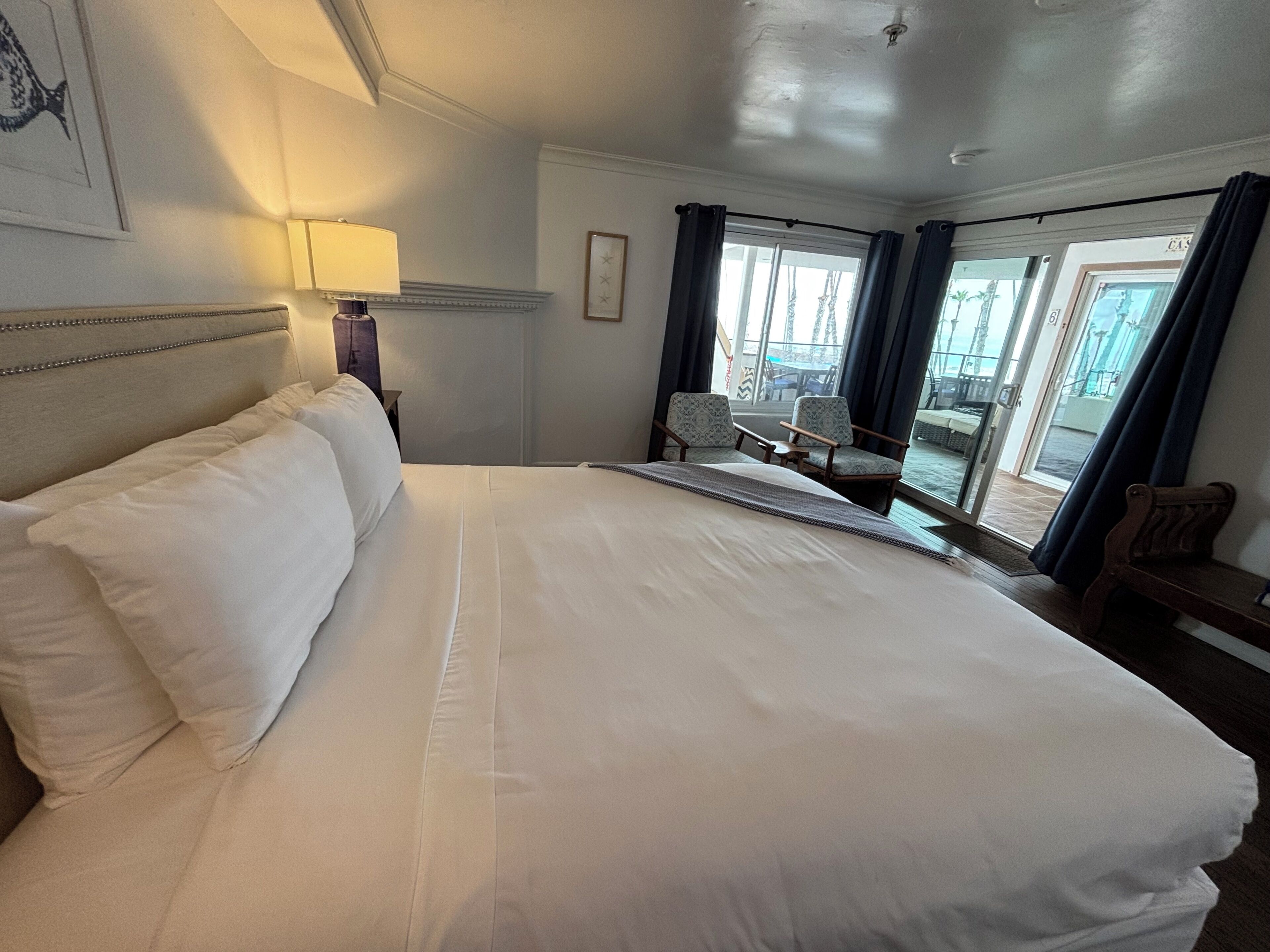 A hotel room with a large bed, a nightstand with a lamp, a chair, and a view of the outside.