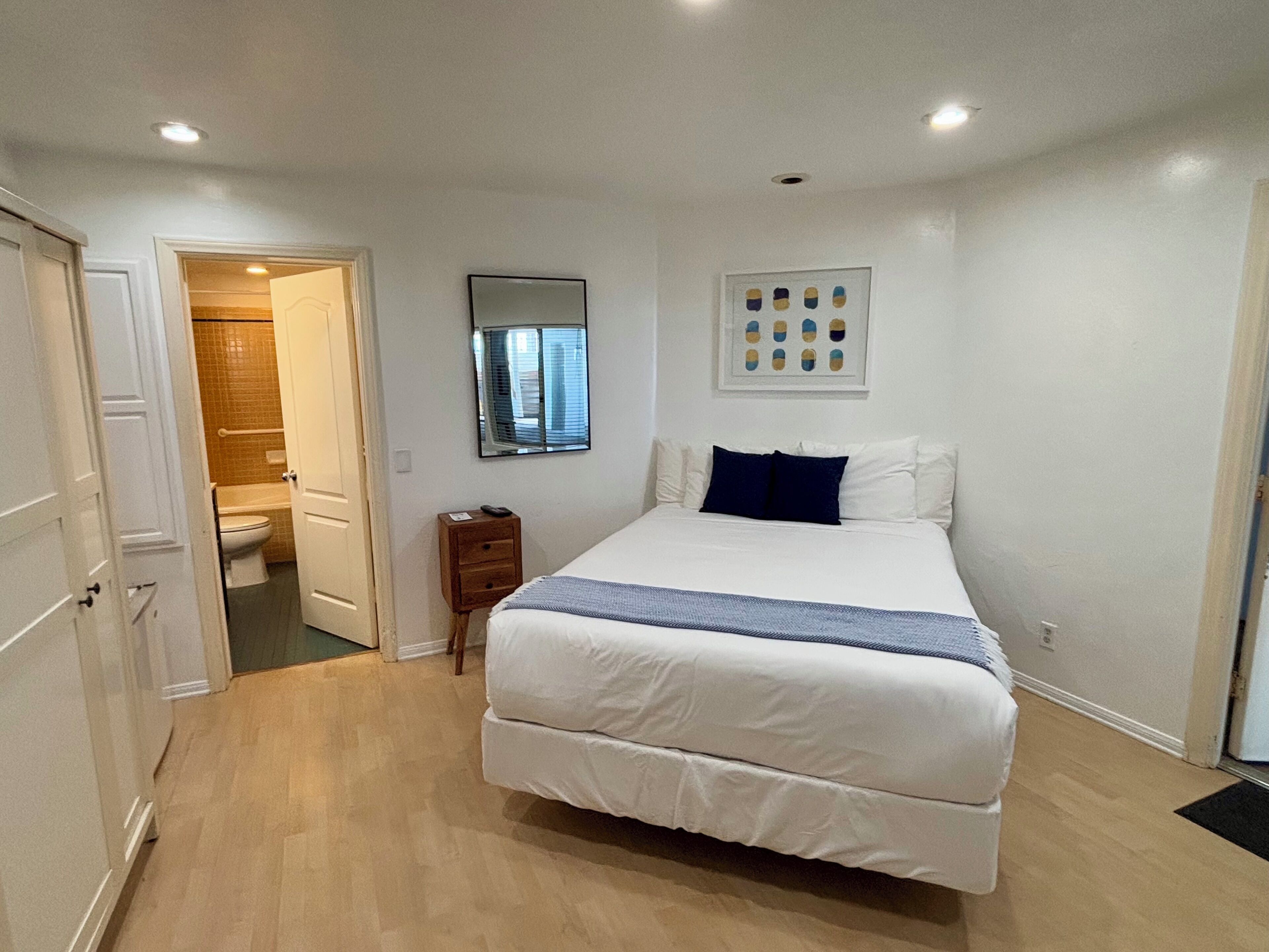 Une chambre à coucher avec un grand lit, une table de chevet, un miroir et un tableau encadré au mur.