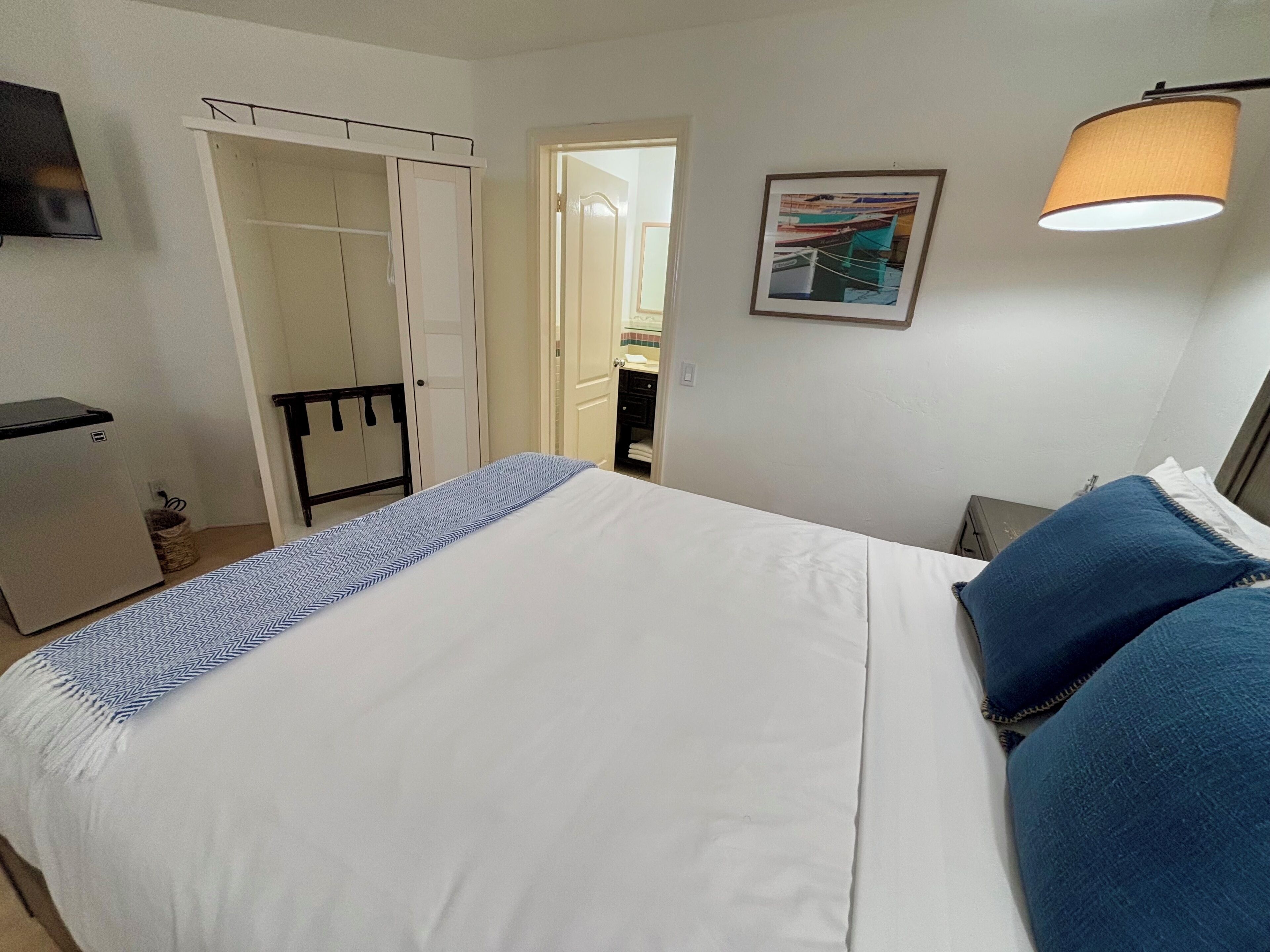 A neatly arranged hotel room with a bed, a wardrobe, a desk, and a lamp.