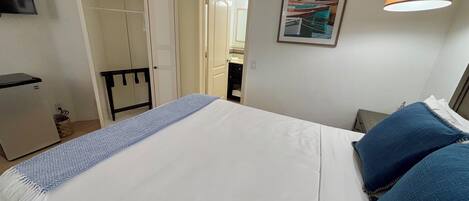 A neatly arranged hotel room with a bed, a wardrobe, a desk, and a lamp.