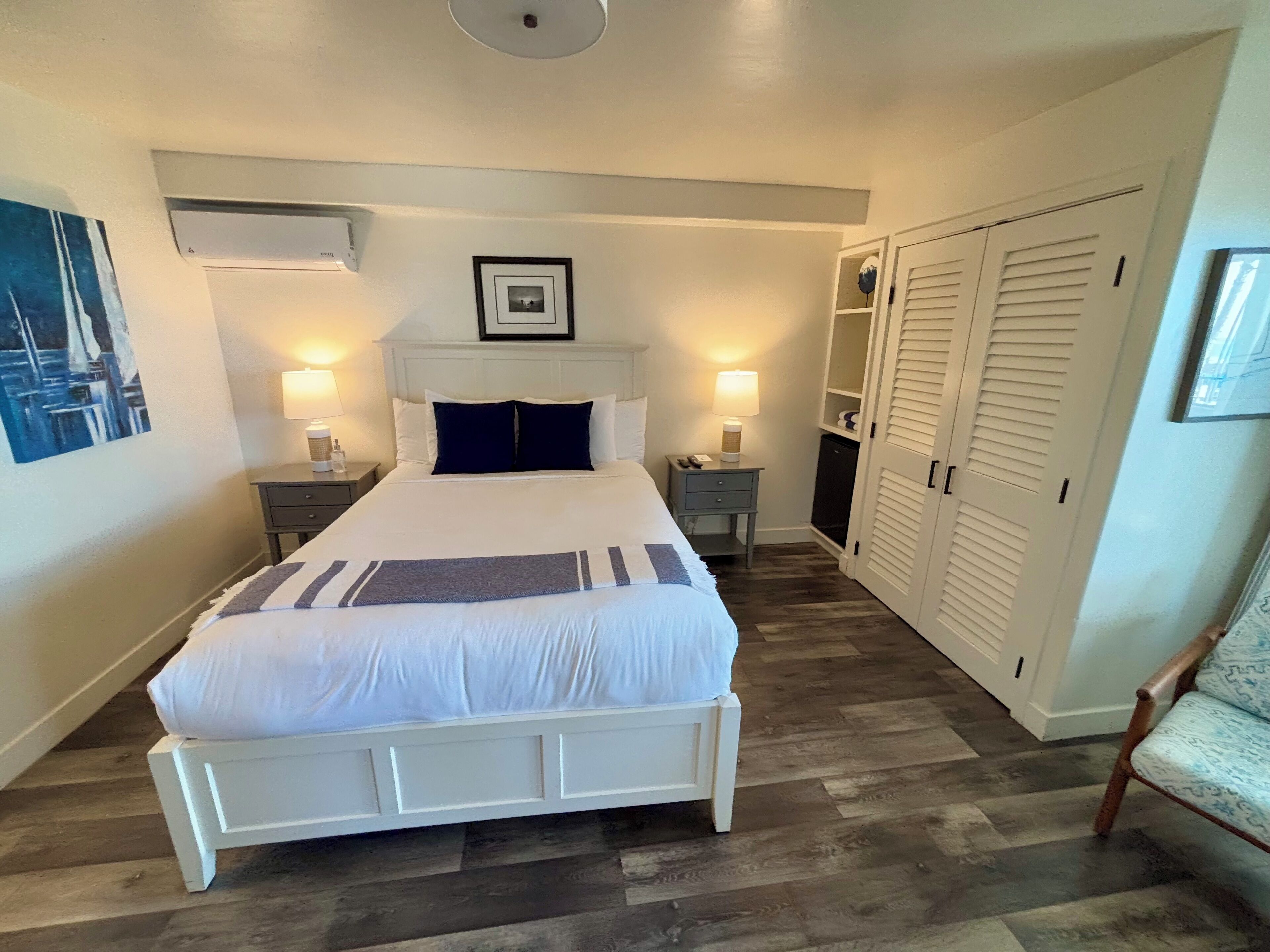 A neatly arranged bedroom with a large bed, bedside tables with lamps, a wardrobe, and a framed picture on the wall.