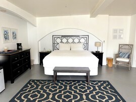 Un dormitorio con una cama grande, un aparador de madera oscura, una mesita de noche, una silla y una alfombra estampada.