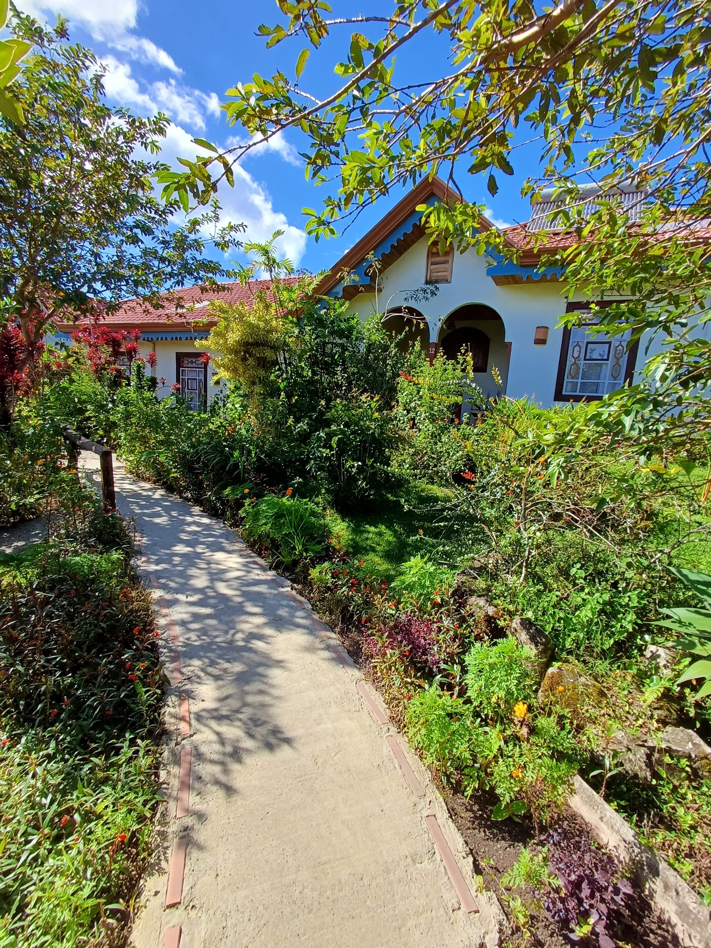 A pathway leading to a building with a red-tiled roof and arched windows.