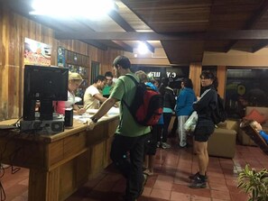 A reception area with a wooden counter, a computer monitor, and a seating area with a couch and a plant. - Coati Place Hostel (Monteverde)