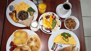 A breakfast table with plates of pancakes, scrambled eggs, toast, and fruit. - Coati Place Hostel (Monteverde)