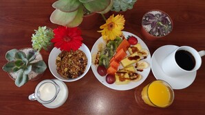A breakfast setting with various food items, a coffee cup, and multiple potted plants on a wooden table. - Coati Place Hostel (Monteverde)