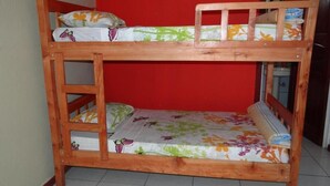 A bunk bed with a ladder, floral bedding, and a red wall in the background. - Coati Place Hostel (Monteverde)