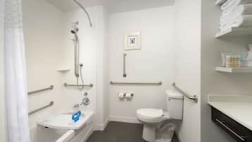 Une salle de bain équipée d’une baignoire, de toilettes et d’une douche. Elle comprend également des barres d’appui et un lavabo accessible aux personnes en fauteuil roulant.