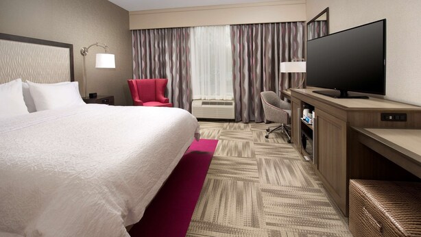 Una habitación de hotel con una cama grande, un televisor de pantalla plana, un escritorio, una silla y una mesita.
