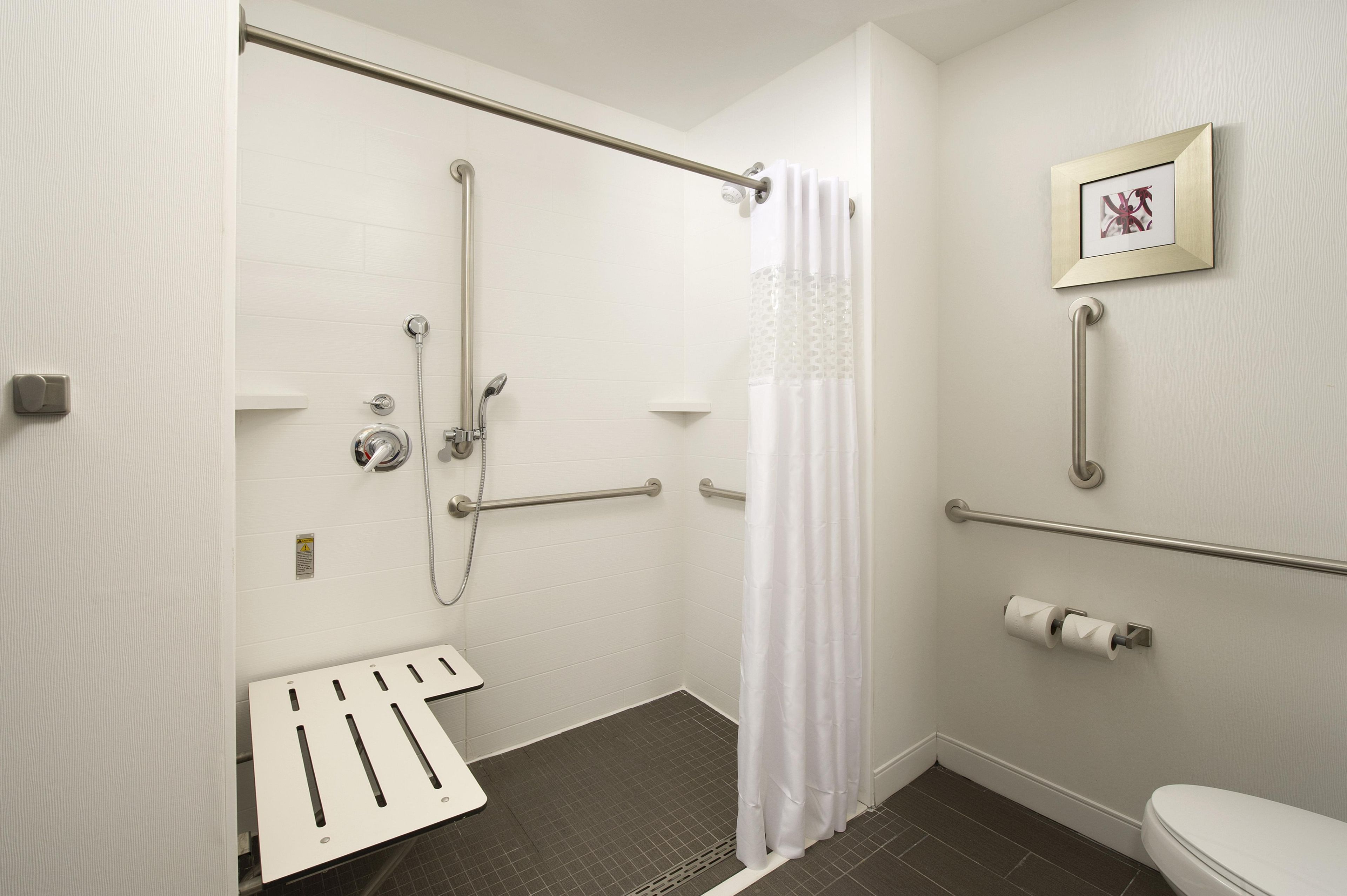 A bathroom with a shower, toilet, and handrails.