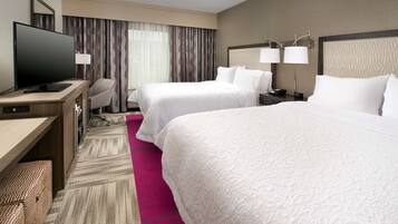A hotel room with two beds, a desk with a television, and a chair.