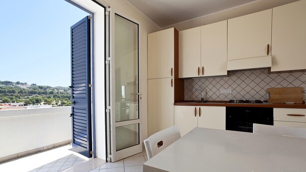 A modern kitchen with a dining area, a sliding glass door to a balcony, and a view of the landscape. - Casa del Sole Trilo A (Castrignano del Capo)