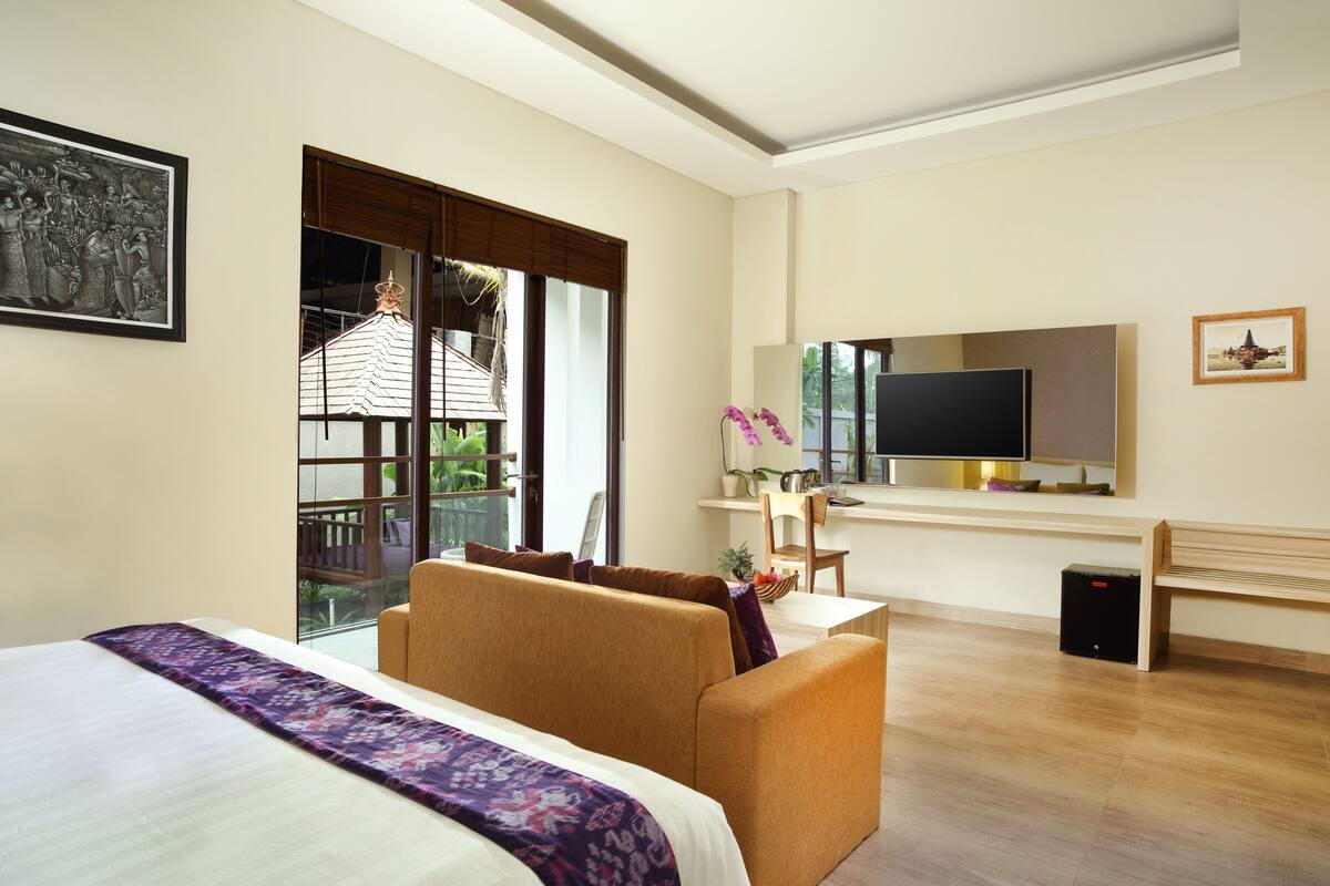 A hotel room with a bed, a sofa, a TV, a desk, and a window with a view of a building.