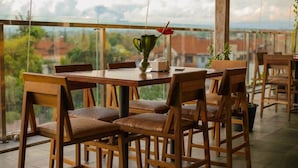 A wooden dining table with six chairs, a vase with a flower, and a view of buildings through a glass railing. - The Evitel Resort Ubud (Ubud)