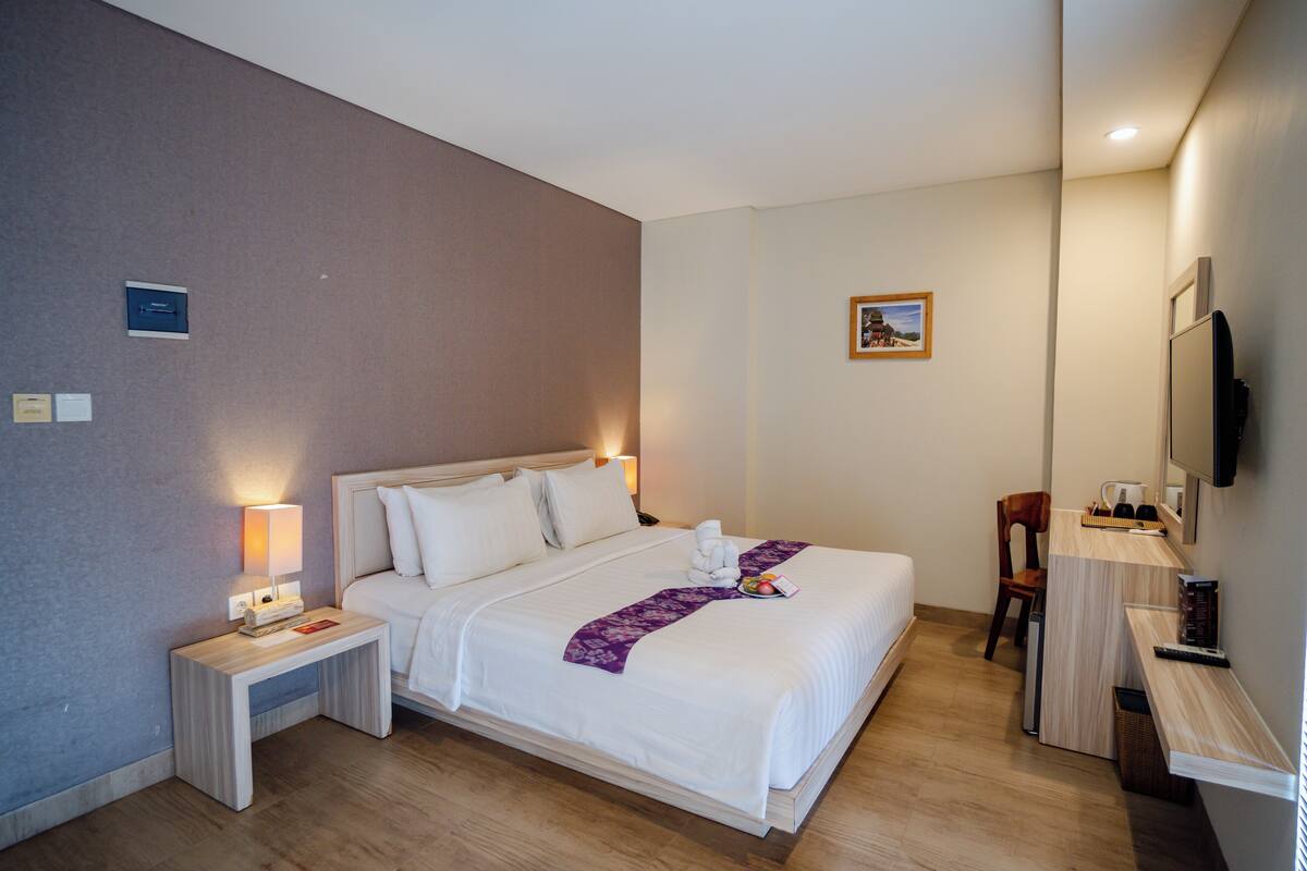 A hotel room with a large bed, bedside tables, a desk, a chair, a television, and a small picture on the wall.