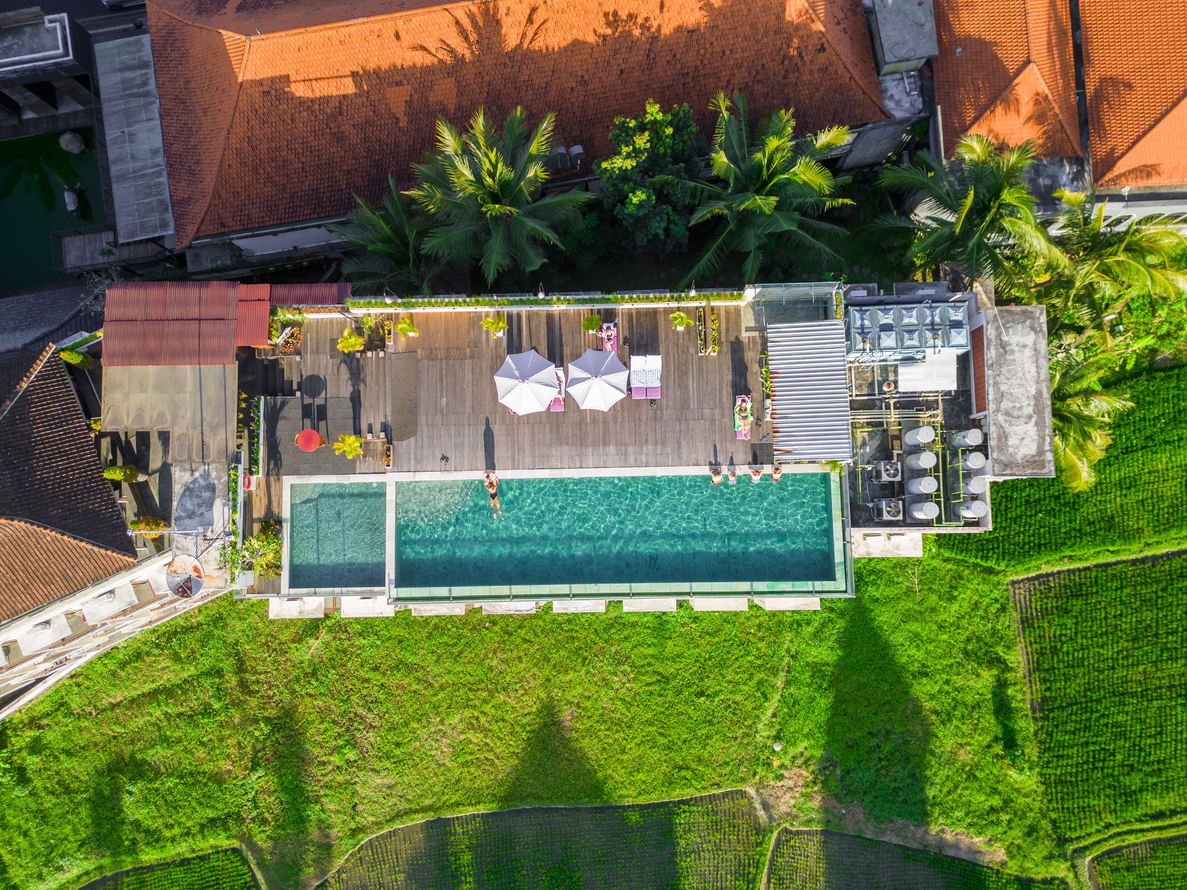 An aerial view of a resort with a swimming pool, lounge area, and lush greenery.